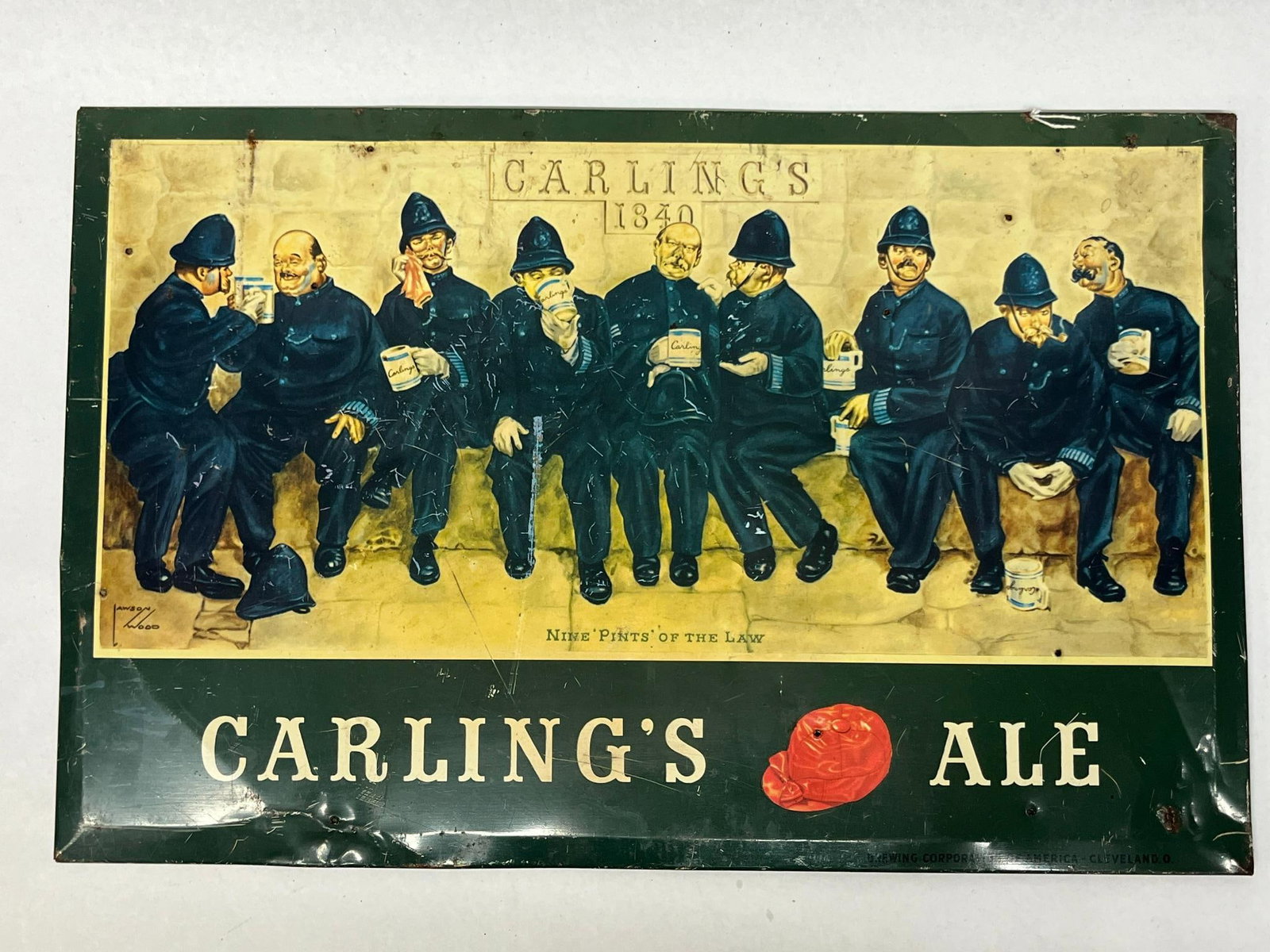 Carling's 9 Pints of Law Tin Litho Sign: This advertising sign is a tin lithograph for Carling's Ale, featuring a humorous illustration by artist Lawson Wood. A printed signature for the artist is visible within a rectangular box in the