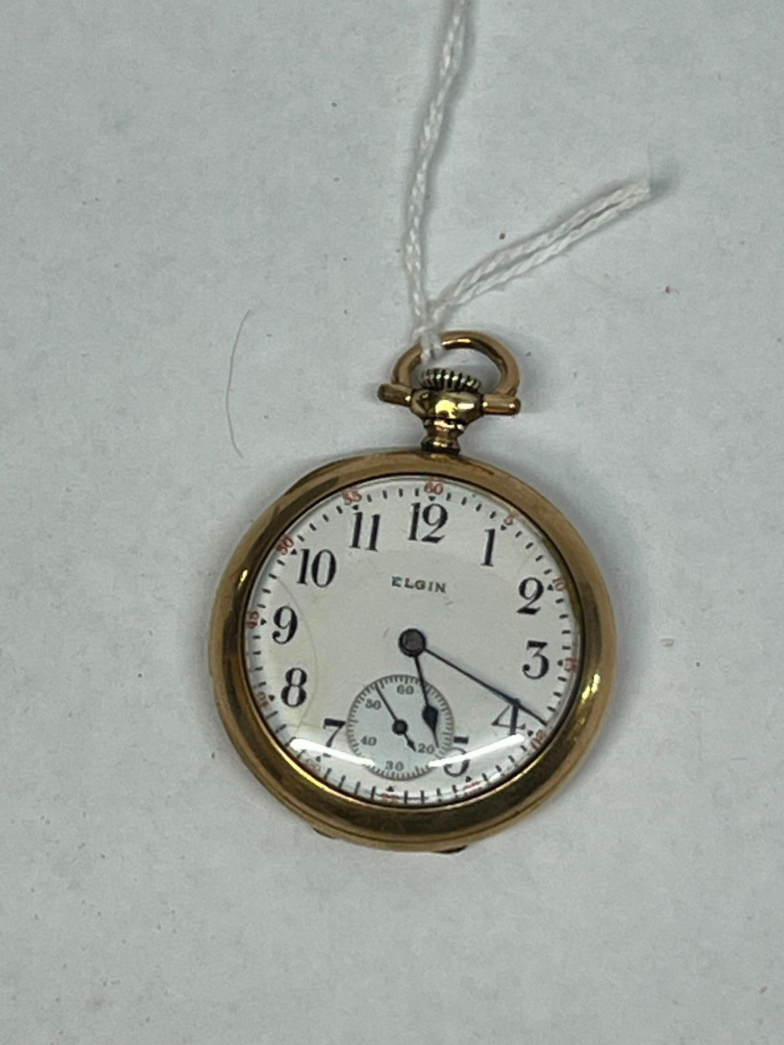 Elgin 7-Jewel Gold-Filled Pocket Watch: An open-face pocket watch manufactured by the Elgin National Watch Co. The watch features a white porcelain or enamel dial with black Arabic numerals, a sub-seconds dial at the 6 o'clock position,