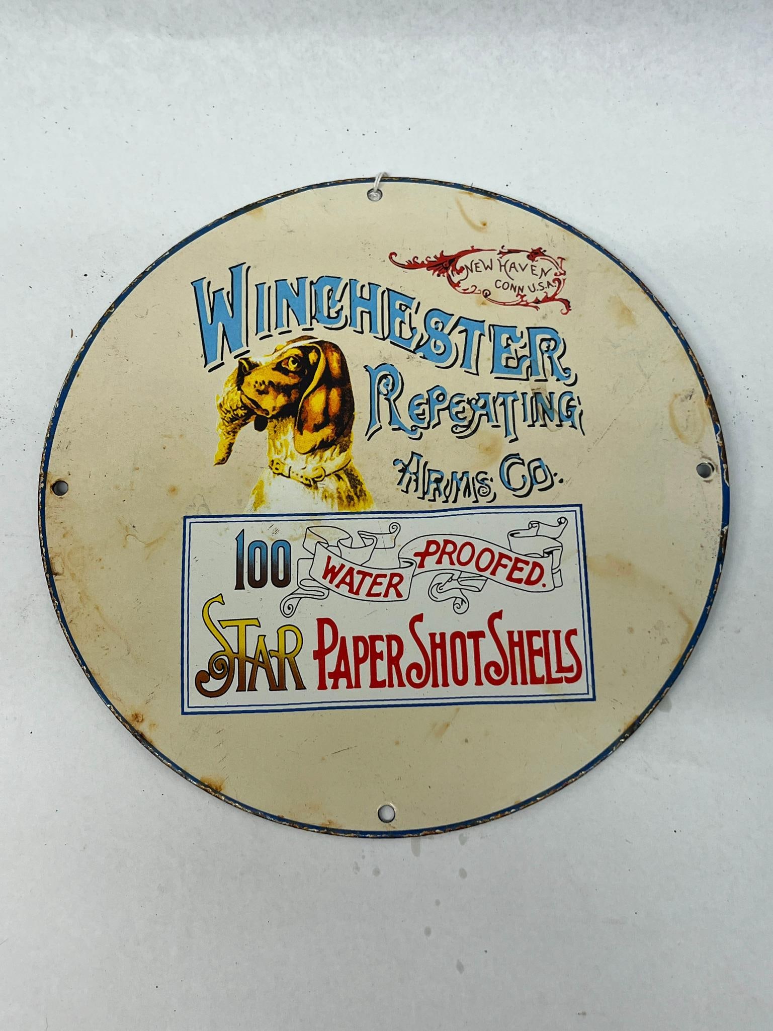 Winchester Star Shot Shells Porc. Sign: A circular porcelain enamel advertising sign produced for the Winchester Repeating Arms Company. The top portion of the sign displays stylized blue and black lettering that reads WINCHESTER Repeating