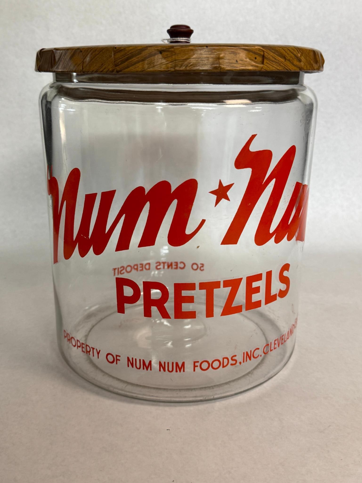 Num Num Foods Inc Advertising Glass Pretzel Jar: This commercial store display jar is constructed of clear glass and features red applied color labeling. A line of text along the lower perimeter reads PROPERTY OF NUM NUM FOODS, INC. The container