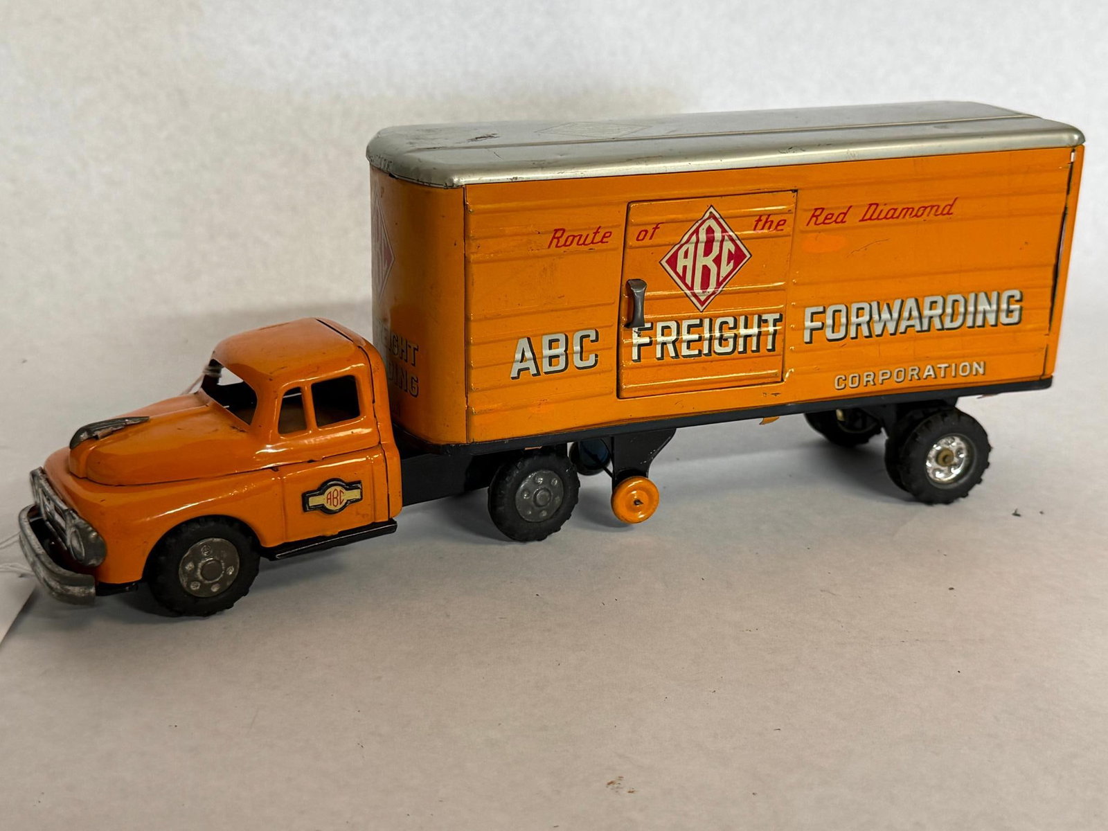 1950s Tin ABC Freight Truck & Trailer: This toy tractor-trailer set is finished in a vibrant orange color scheme. The trailer is constructed of lithographed tin and features the commercial livery of the ABC Freight Forwarding Corporation.