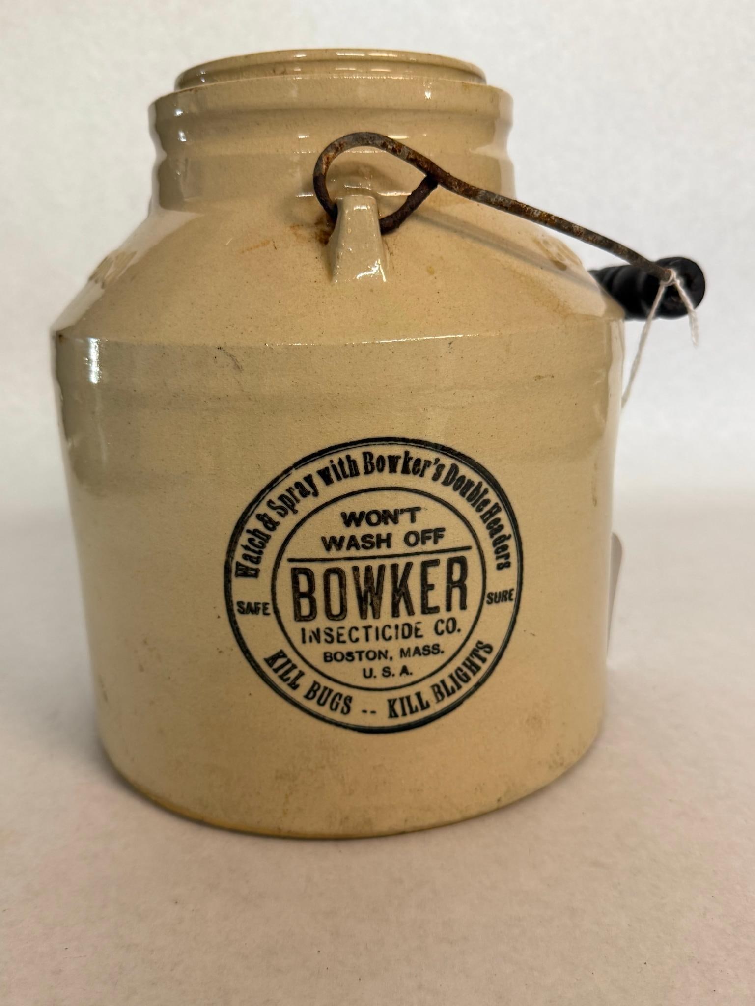 Bowker Insecticide Stoneware Poison Jar: This cylindrical stoneware insecticide jar is finished in a tan glaze with a dark brown slip-glazed interior. A circular black transfer-printed label on the front reads Watch & Spray with Bowker's