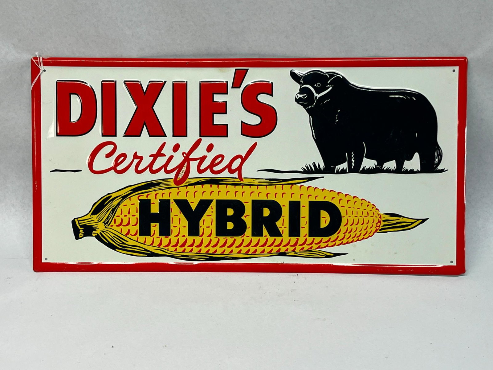 Dixie's Embossed Metal Seed Corn Sign: A rectangular embossed sheet metal sign advertising Dixie's Certified Hybrid seed corn. The text DIXIE'S is printed in large red block letters with black outlines at the top left, with the word