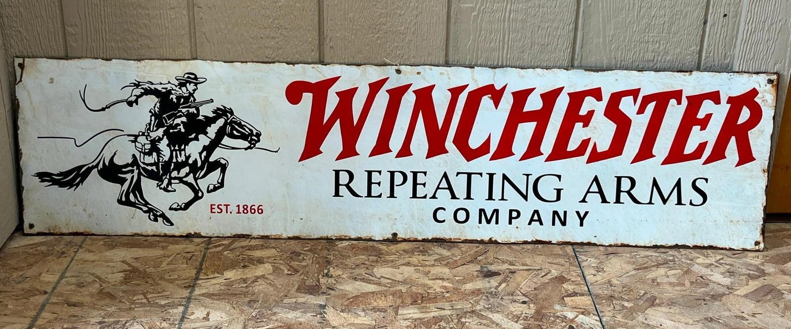 Winchester Repeating Arms Metal Sign: A large format, rectangular advertising sign composed of painted sheet metal. To the left is a black silhouette graphic of the horse and rider logo, depicting a figure on a galloping horse with a