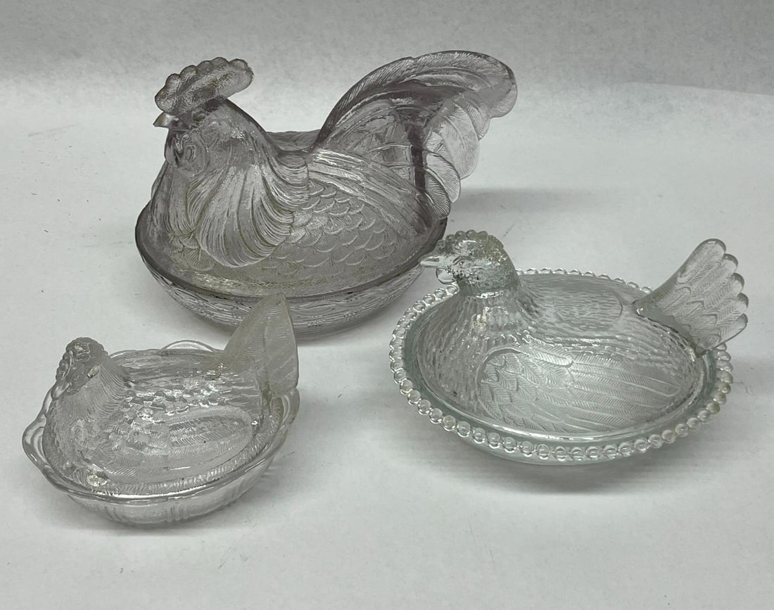 Trio Pressed Glass Hen & Rooster Nests: This lot consists of a trio of clear pressed glass covered dishes modeled in the traditional poultry on nest form. The underside of this base features an impressed mark in a central oval consisting