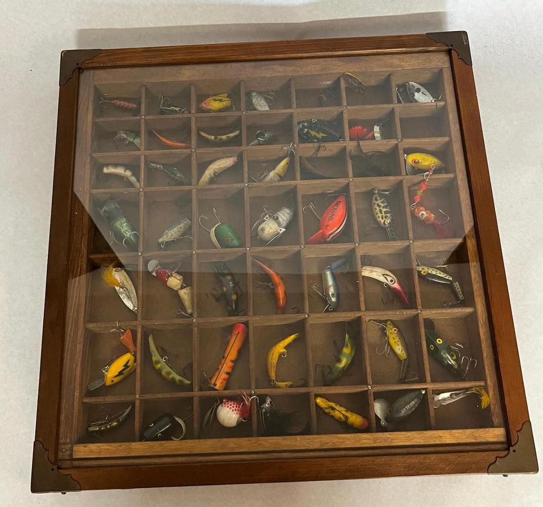 Fishing Lures in Wood Display Case: An assortment of and antique fishing lures presented in a rectangular wooden display case. The case features a glass top, decorative metal corner brackets, and is divided into forty-two individual