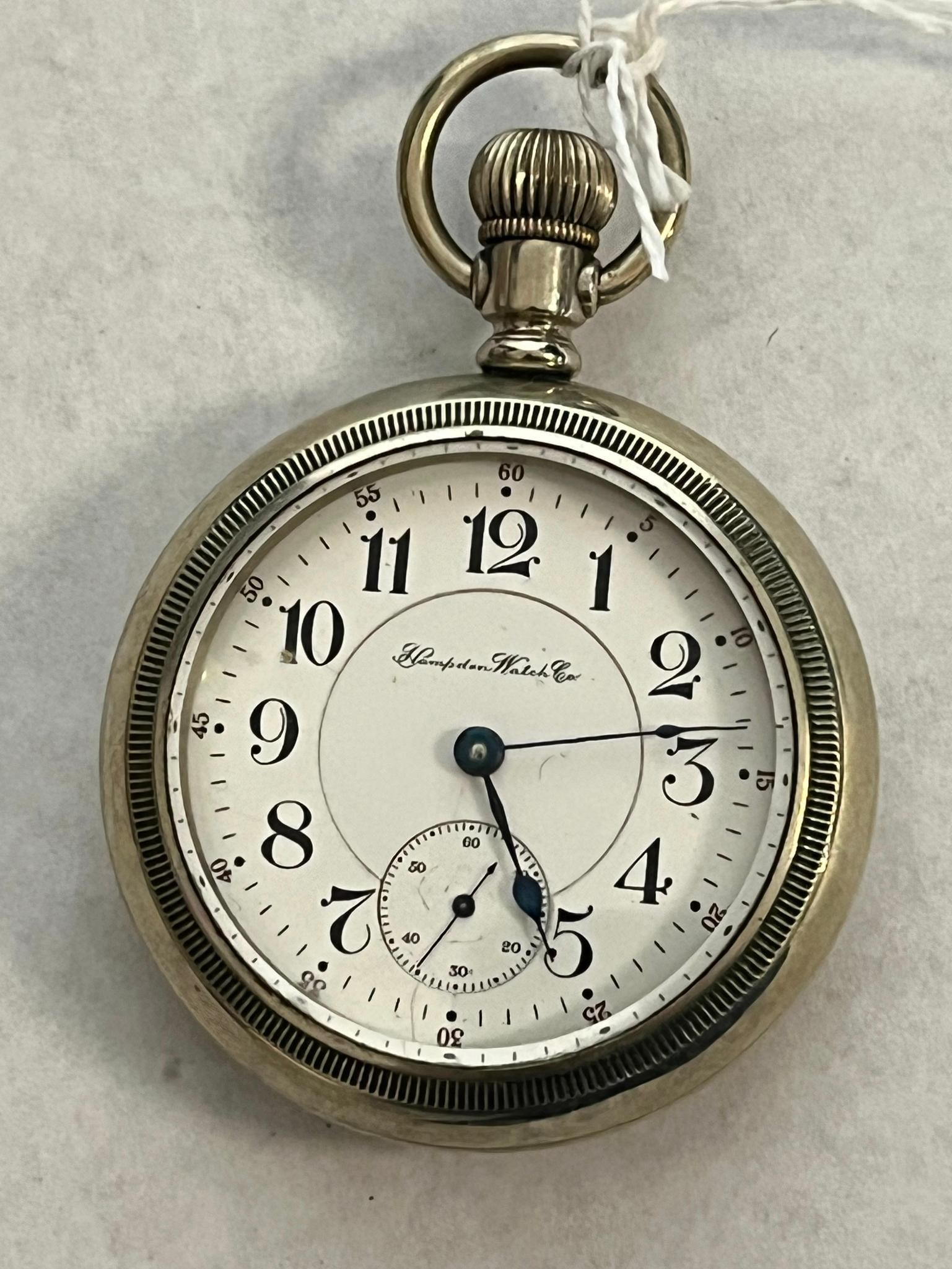 Hampden New Railway Nickel Pocket Watch: An open-face pocket watch manufactured by the Hampden Watch Co. Features a white porcelain enamel dial bearing the cursive script mark Hampden Watch Co. The hands are crafted from blued steel in a