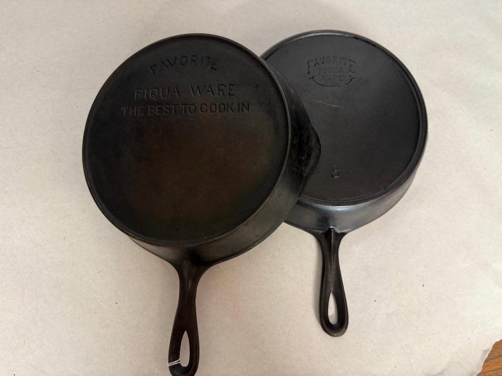 Pair Favorite Piqua Ware No. 8 Skillets: This lot consists of two antique cast iron skillets manufactured by the Favorite Stove and Range Company of Piqua, Ohio. The first skillet features a block-letter logo impressed on the base with the