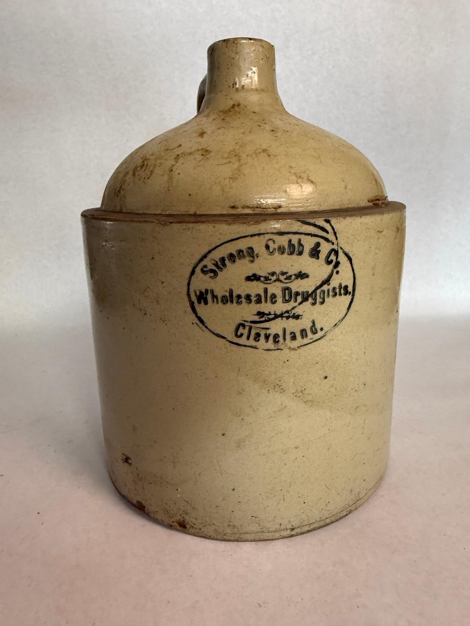 Strong Cobb & Co Stoneware Shoulder Jug: An antique stoneware shoulder jug constructed with a cylindrical body and a single loop handle attached at the neck. Centered on the front of the body is a black transfer-printed mark inside an oval
