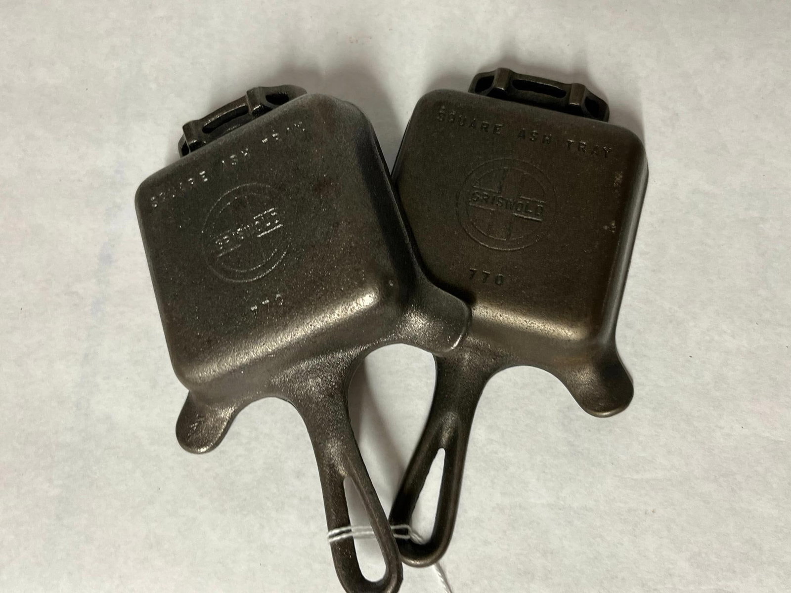 Pair Griswold 770 Cast Iron Ashtrays: A pair of cast iron ashtrays designed in the form of small square skillets. On the underside of each base, the text SQUARE ASH TRAY is cast in relief above a circular logo containing a cross with the