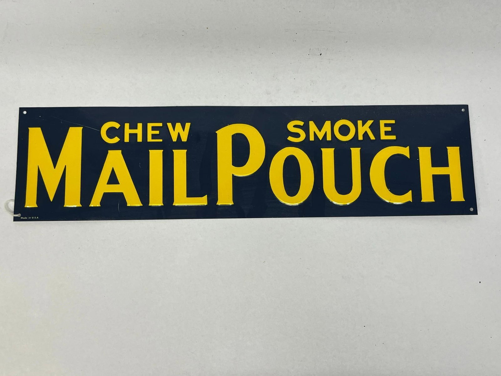 Mail Pouch Tobacco Embossed Metal Sign: An American horizontal rectangular advertising sign for Mail Pouch tobacco. The sign is constructed from embossed metal featuring raised lettering. The design consists of a dark navy blue ground with