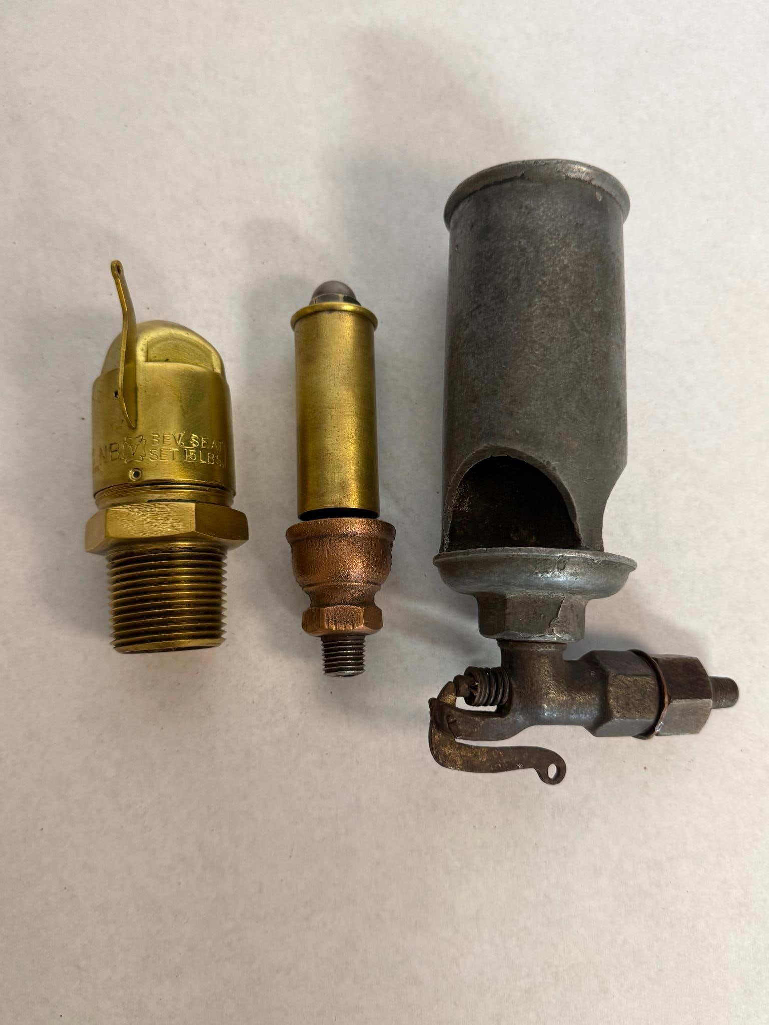3 Antique Steam Whistles & Safety Valve: This lot comprises a collection of three antique industrial components typically used in steam or pneumatic systems, featuring brass, copper alloy, and iron construction. The first item is a brass