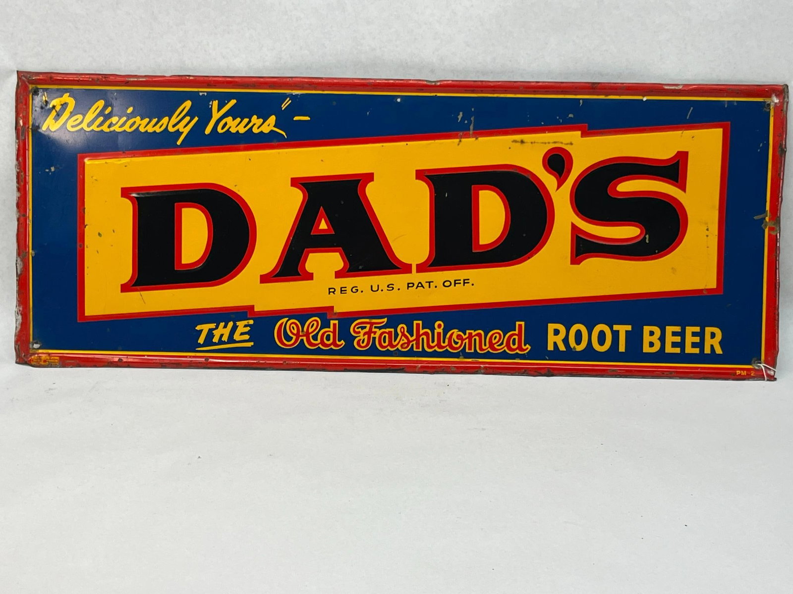 Dad's Root Beer Embossed Tin Litho Sign: A embossed tin lithograph advertising sign for Dad's Root Beer. Directly below the brand name is the printed text REG. The lower left corner features a red and yellow decal for the union label reading