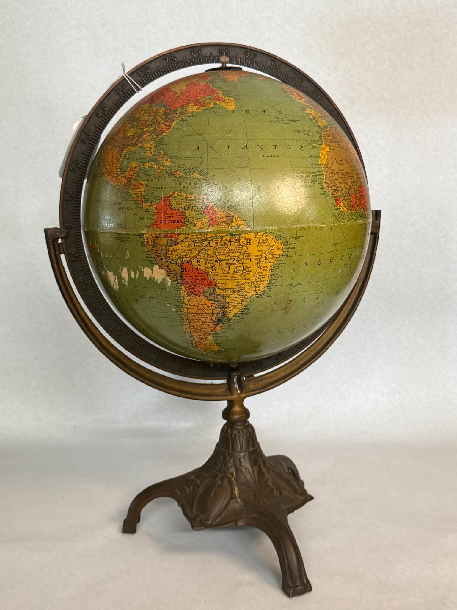 Replogle Globe on Cast Metal Tripod: An American tabletop terrestrial globe featuring lithographed paper gores applied to a central sphere. A printed legend located in the Pacific Ocean features a logo of an eagle with wings spread