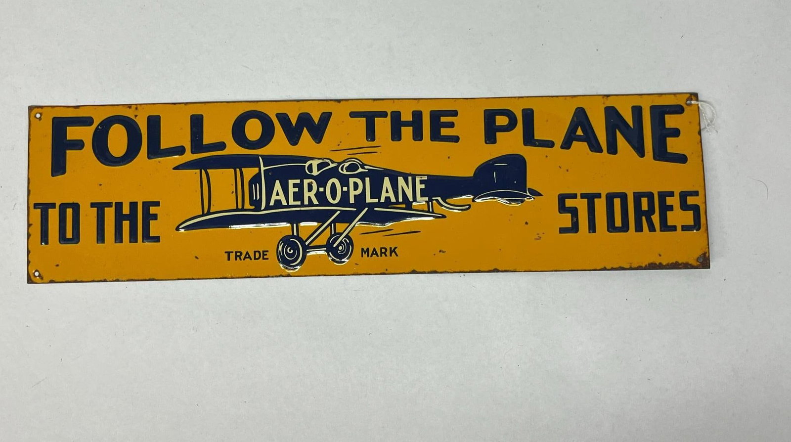 Aer-O-Plane Stores Embossed Tin Sign: A rectangular advertising sign for Aer-O-Plane Stores, constructed from stamped embossed tin with a lithographed finish. Small printed text reading TRADE MARK is positioned directly beneath the landin