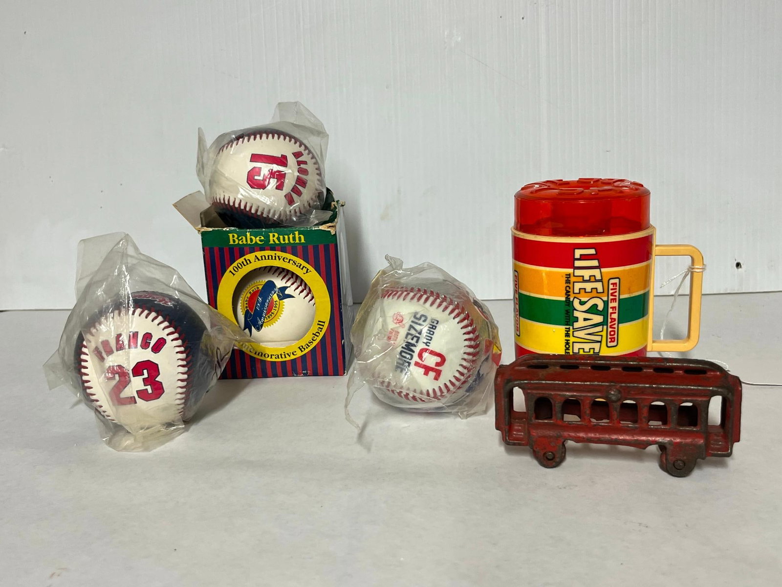 Baseballs, Deka Mug & Iron Streetcar: A collection consisting of four commemorative baseballs, one promotional plastic mug, and a cast iron toy vehicle. The sports memorabilia includes a Babe Ruth 100th Anniversary Commemorative