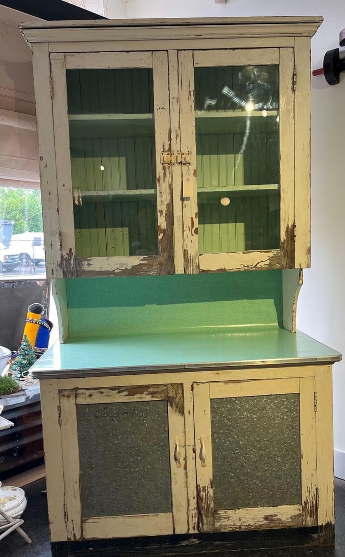 Distressed Wood & Metal Kitchen Hutch: A two-piece kitchen hutch of wooden construction featuring a heavily distressed cream-colored painted exterior over a green interior. The upper unit is configured with two doors, each inset with a sin