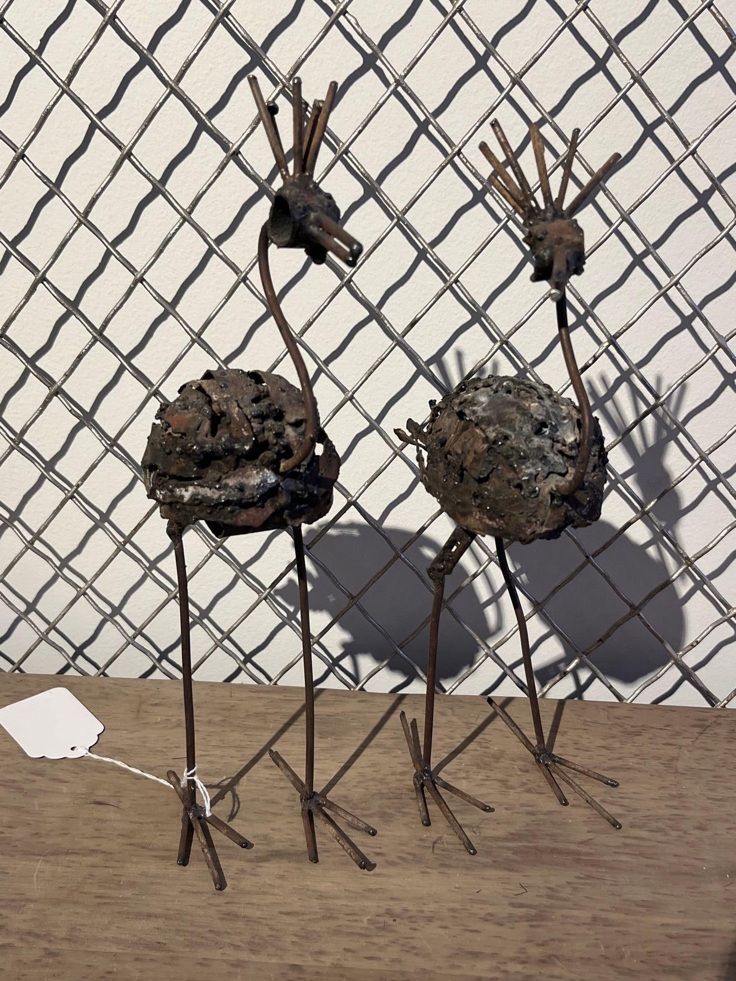 Pair Welded Scrap Metal Bird Sculptures: A pair of welded scrap metal sculptures of stylized avian figures, resembling crested cranes or ostriches. These works are constructed from salvaged iron or steel components, featuring bodies made of