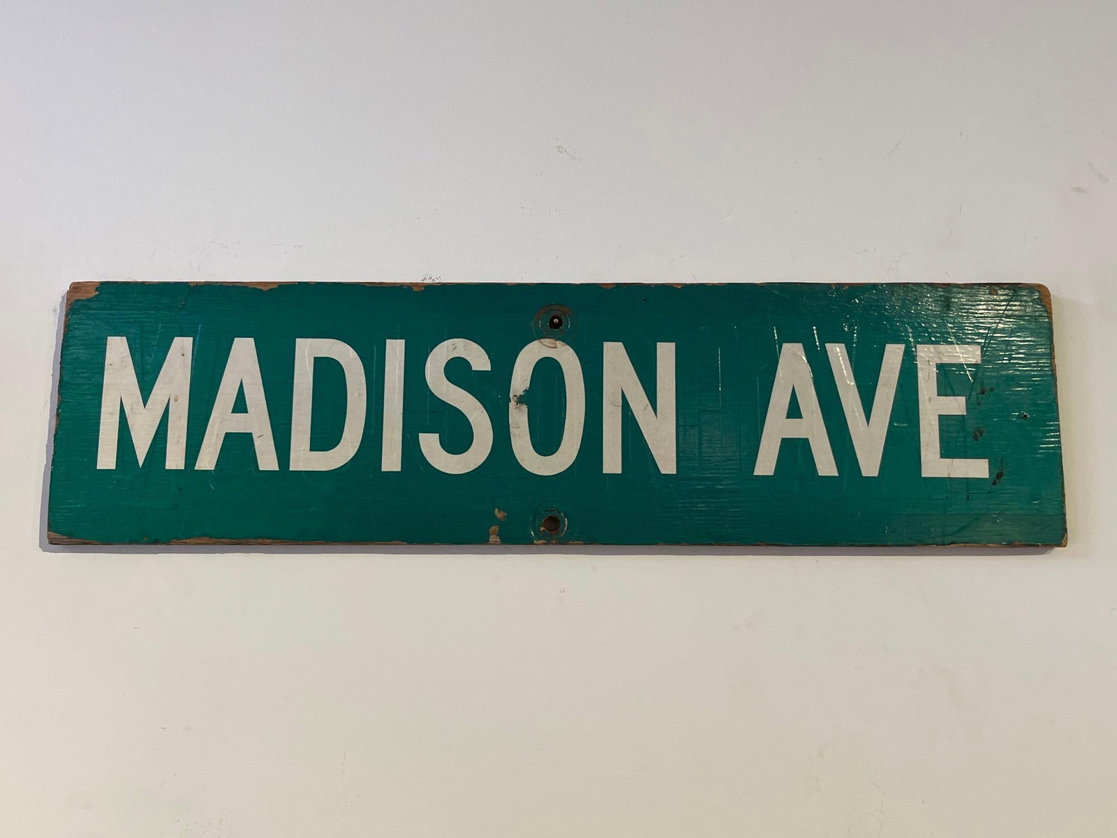Painted Wood Madison Avenue Sign: This street sign features the text MADISON AVE in bold white block capital letters against a dark forest green painted background. The sign is constructed from a single rectangular piece of wood or