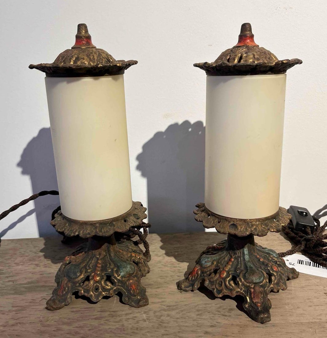 Pair Polychrome Cast Metal Table Lamps: A pair of electrified table lamps, each featuring an ornate pierced metal base and matching top cap with a cylindrical white milk glass shade. The footed bases and domed caps are cast metal with a pol