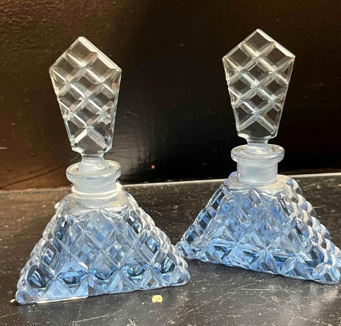 A Pair of Art Deco Style Aquamarine Cut Glass Perfume Bottles: A pair of matching aquamarine blue cut glass perfume bottles. Each vessel is crafted with a three-sided pyramidal body and a tall, flat, shield-shaped stopper. The bodies and stoppers are decorated
