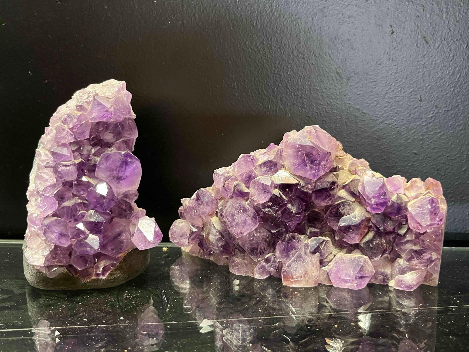 Pair Amethyst Crystal Cluster Specimens: A lot of two natural amethyst quartz crystal clusters, presented as geode sections. The first specimen is an upright, vertical formation featuring a dense bed of deep purple crystals with sharp pyrami