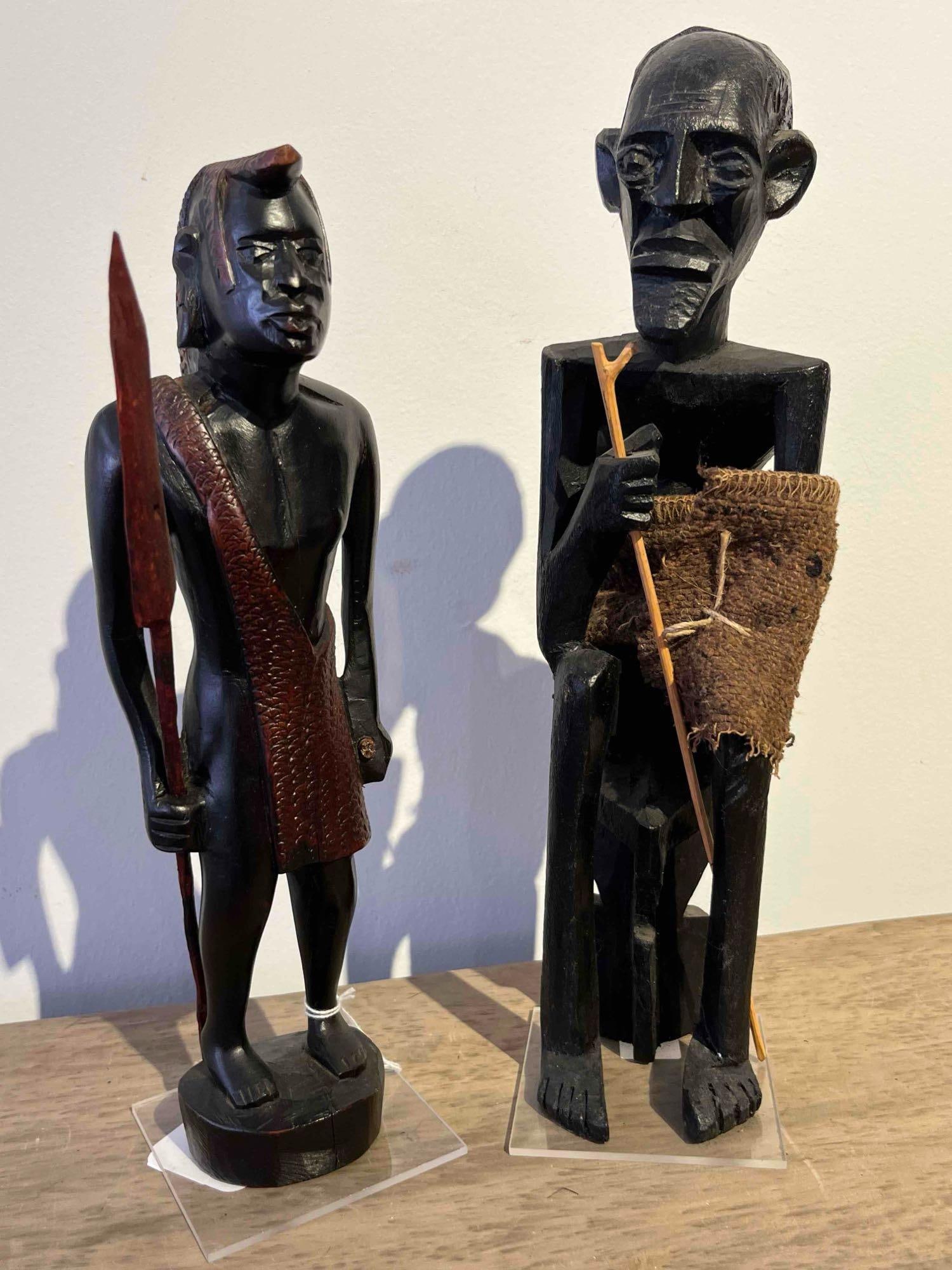 Pair African Hardwood Tribal Figures: This pair of hand-carved representational sculptures is crafted from a dense, heavy hardwood with a dark finish. The collection consists of two distinct archetypal figures: a warrior and an elder. The