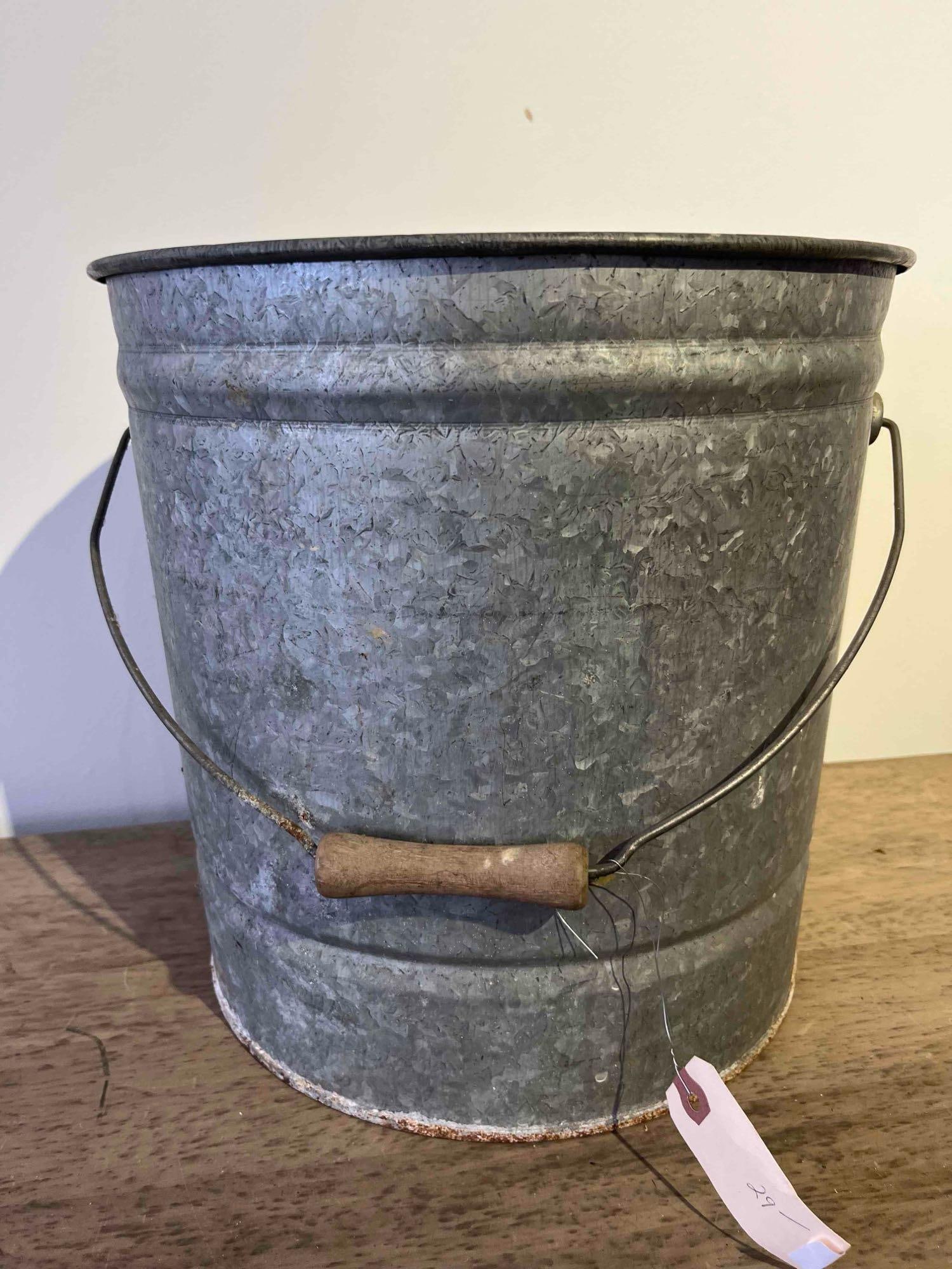Wheeling Corrugating Steel Pail: This mid-20th century industrial style pail is constructed of galvanized steel with a wire handle and a turned wooden grip. A rectangular metal plate is riveted to the upper rim and contains the