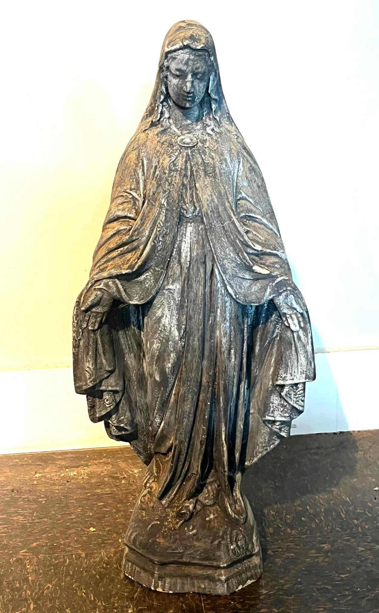 Cast Composite Virgin Mary Sculpture: This standing sculpture depicts the Virgin Mary in the traditional iconographic pose of Our Lady of Grace, characterized by open, downturned hands. The figure is rendered in a layered ensemble