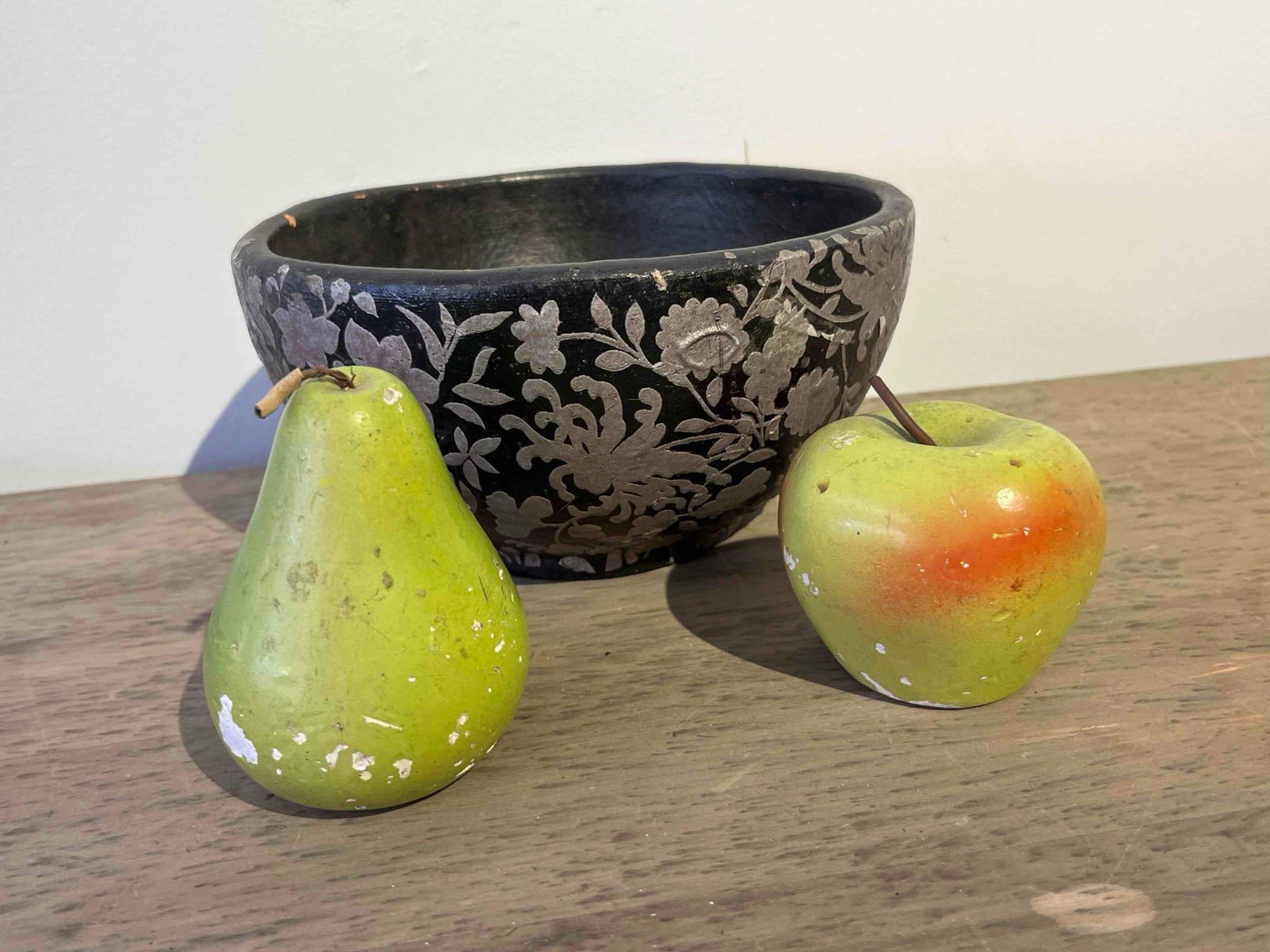 Lacquered Floral Bowl & Stone Fruit: A round decorative bowl and two pieces of hand-painted stone fruit. The bowl is crafted from a composite material, likely paper-m?ch?, with a black lacquer-style finish and raised silver-toned floral 