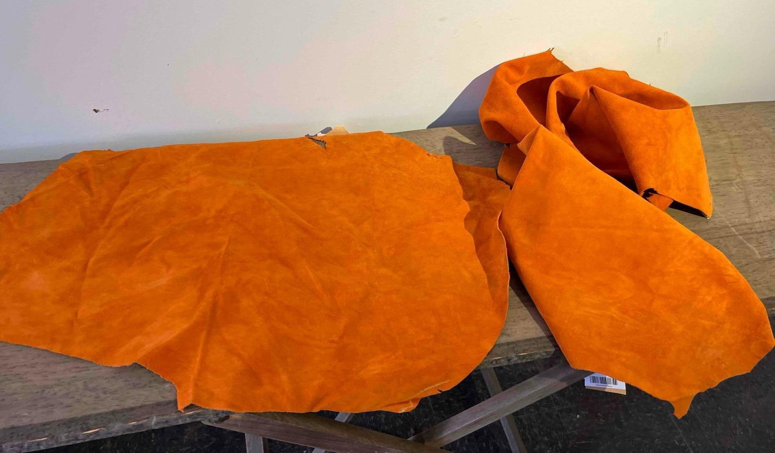 A Pair of Orange Sueded Hog Leather Hides: This lot consists of two loose orange leather pigskin hides intended for craft, hobby, or upholstery use. The material features a sueded or nubuck-style finish, providing a soft, matte texture across