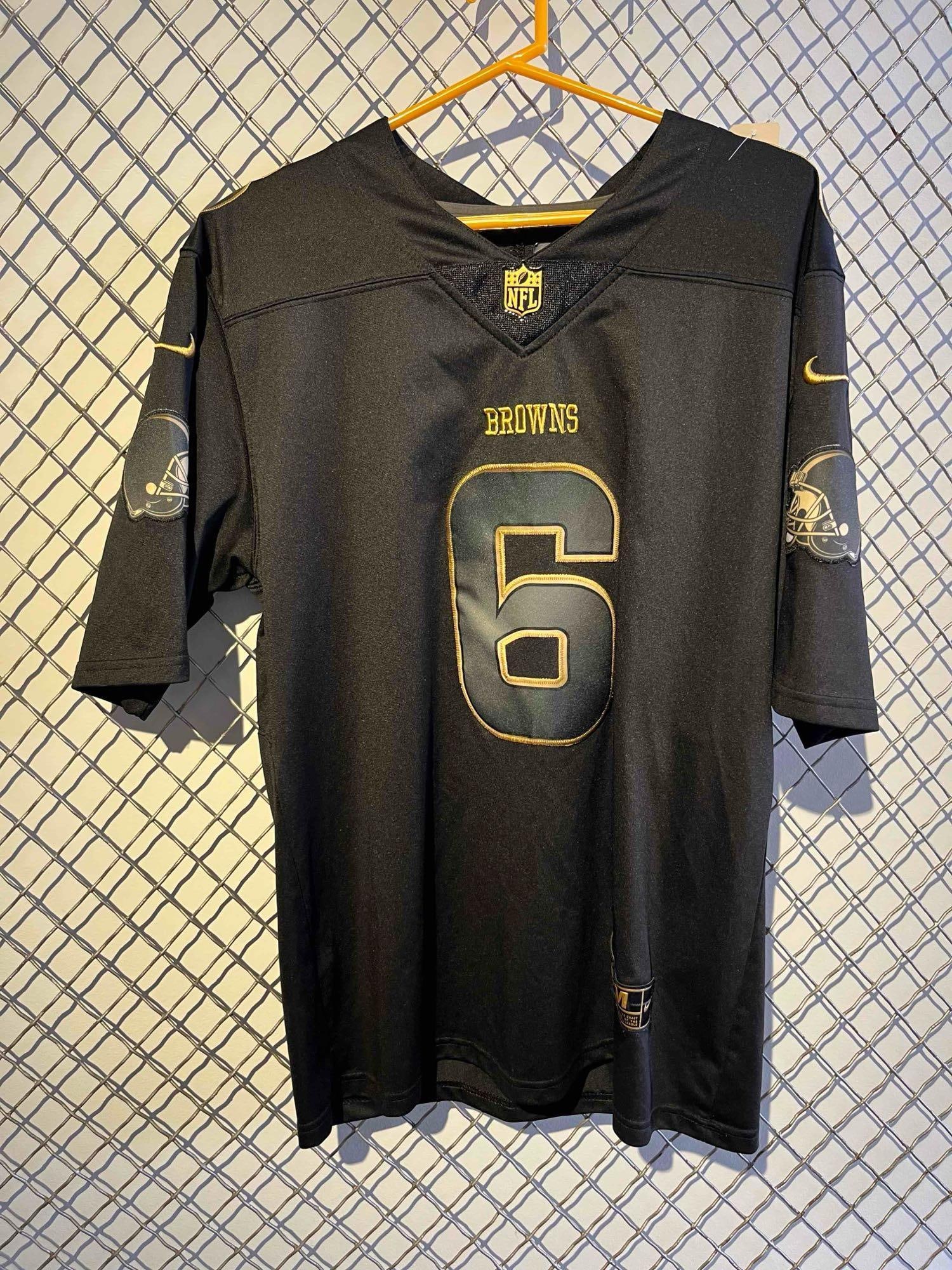 Baker Mayfield Salute to Service Jersey: An NFL football jersey for the Cleveland Browns, featuring the name and number of player Baker Mayfield, number 6. The garment is presented in a black and gold colorway consistent with the Salute to S