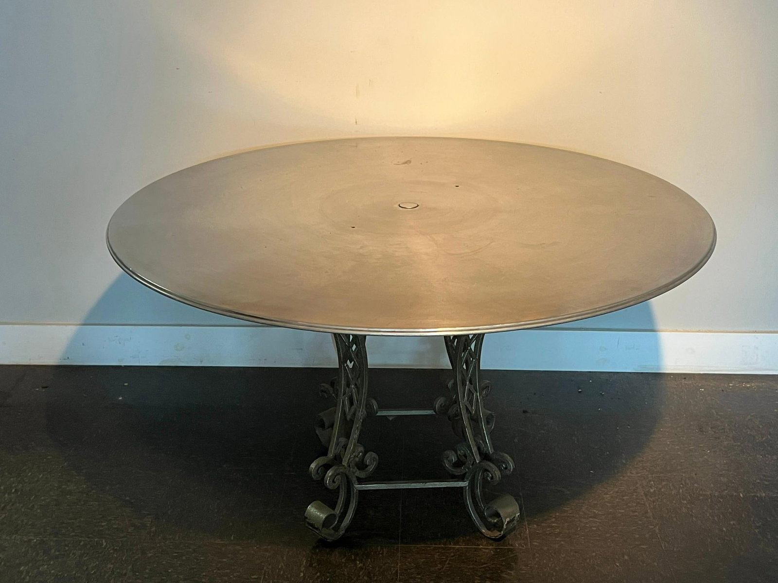 Repurposed Hollywood Take Up Reel Table: A large circular dining table featuring a heavy-gauge metal tabletop supported by a wrought metal pedestal base. This was constructed from a Hollywood take up reel used in Detroit Theater in