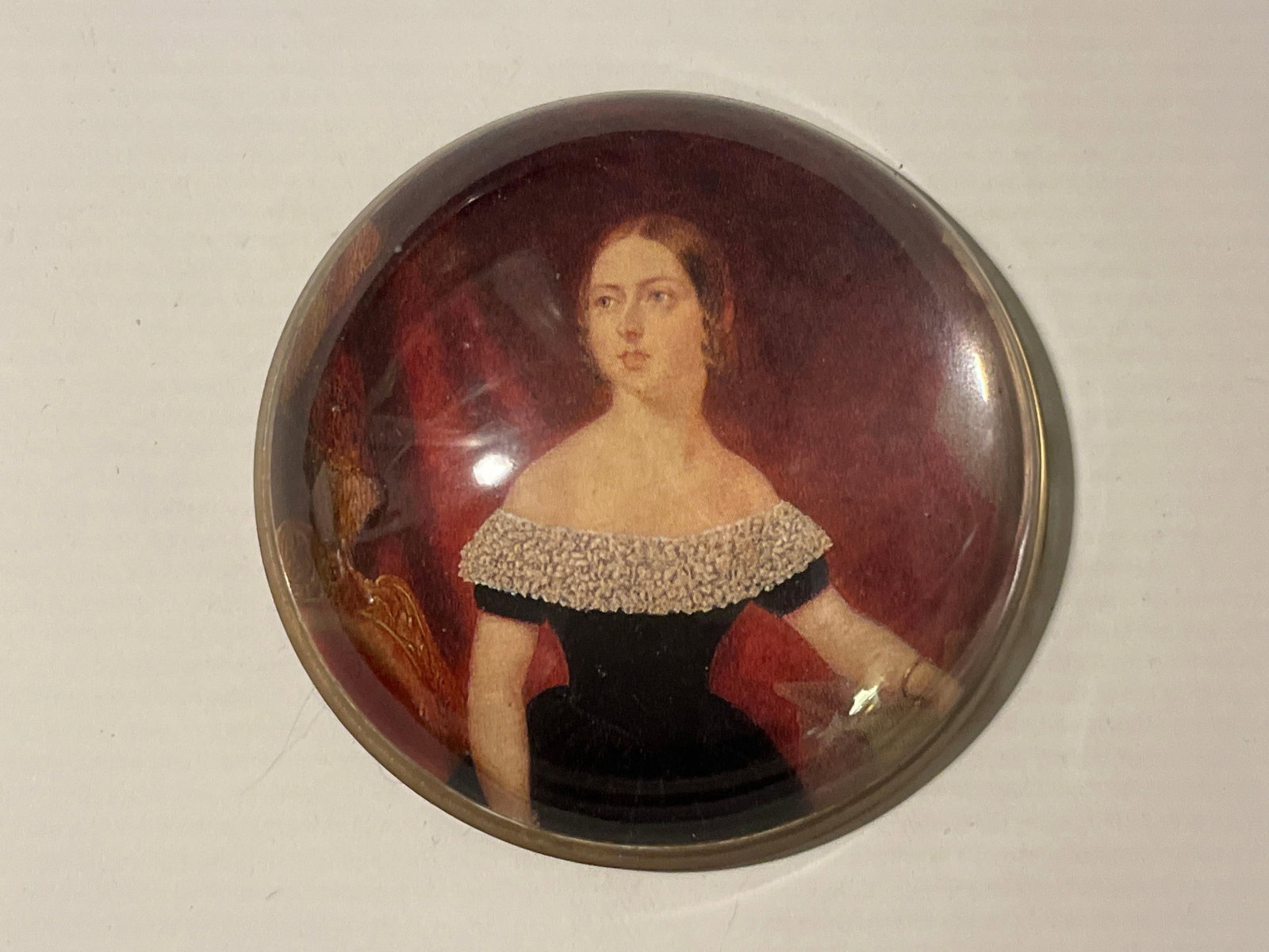 Aaron Penley Victoria Glass Paperweight: An English Nigel Pain Products circular domed glass paperweight featuring a color print reproduction of a portrait of a young Queen Victoria. The subject is depicted in a black gown with a white lace 