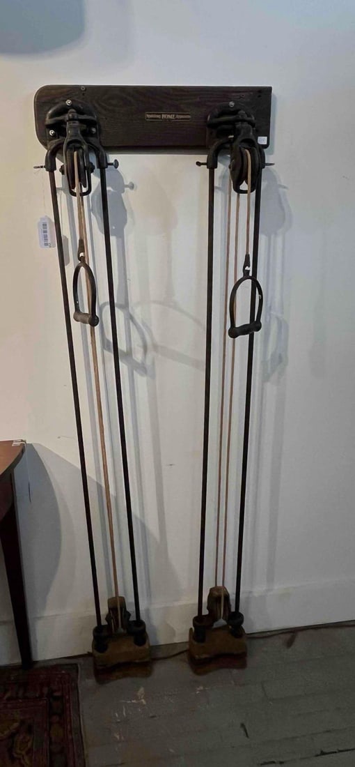 Spalding No. 12 Wall Weight Machine: An dual-pulley home exercise system constructed from cast iron, steel, and stained wood. The apparatus is designed for wall mounting and consists of a dark-stained shaped wooden headboard supporting t