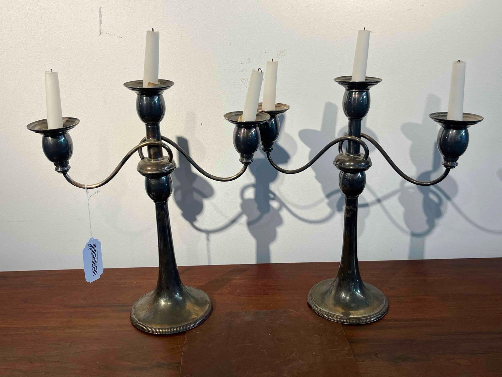 Pair 3-Light Silver-Plated Candelabras: A pair of silver-toned metal three-light candelabras. Each piece consists of a central vertical column topped with a candle cup, flanked by two scrolling arms supporting additional candle cups. The ca