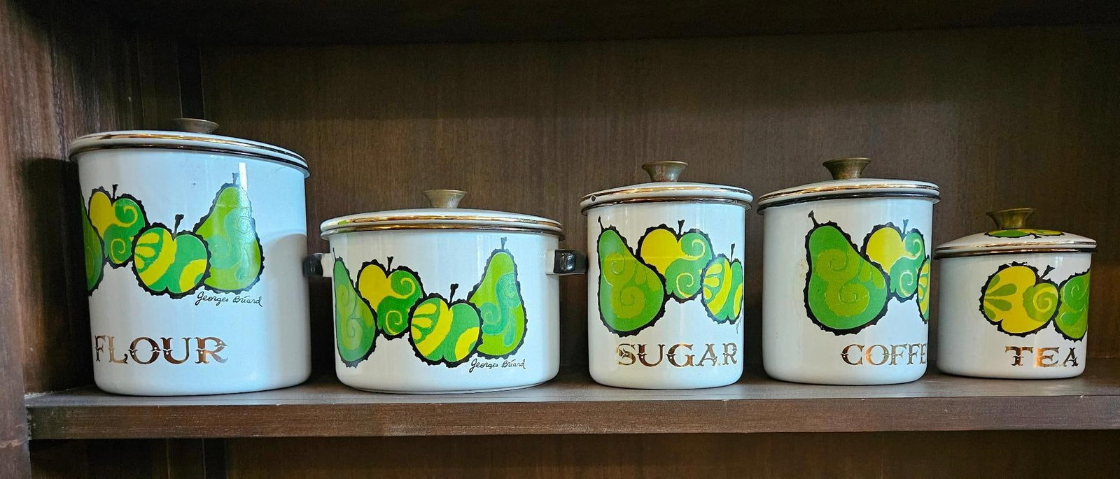 Georges Briard Enameled Canister Set: A five-piece collection of kitchen enamelware comprising a four-piece graduated canister set and a matching lidded Dutch oven. Each piece is constructed from white enameled metal with brass-toned meta