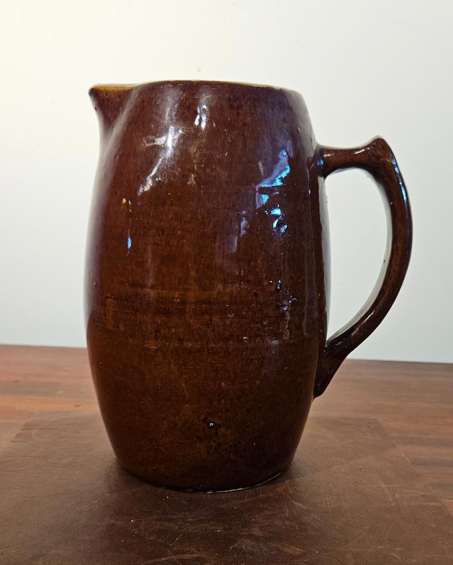 Dark Brown & Cream Stoneware Pitcher: A large utilitarian stoneware pitcher featuring a bulbous ovoid body and an applied handle. The exterior is finished with a glossy dark brown slip glaze, while the interior features a contrasting crea