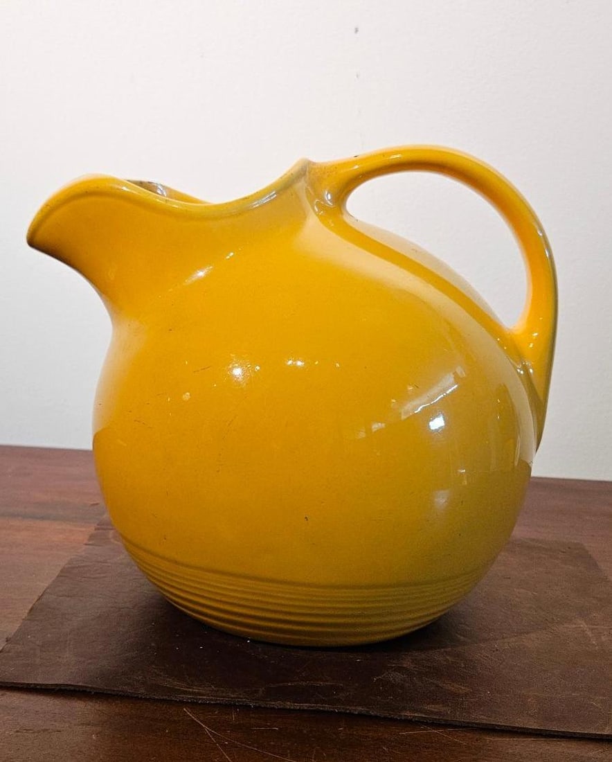 Yellow Glazed Ball Pitcher w/ Ice Guard: A mid-century modern glazed earthenware pitcher featuring a spherical body and an integrated ice-guard spout. The vessel is finished in a vibrant, solid yellow glossy glaze. The lower portion of the b