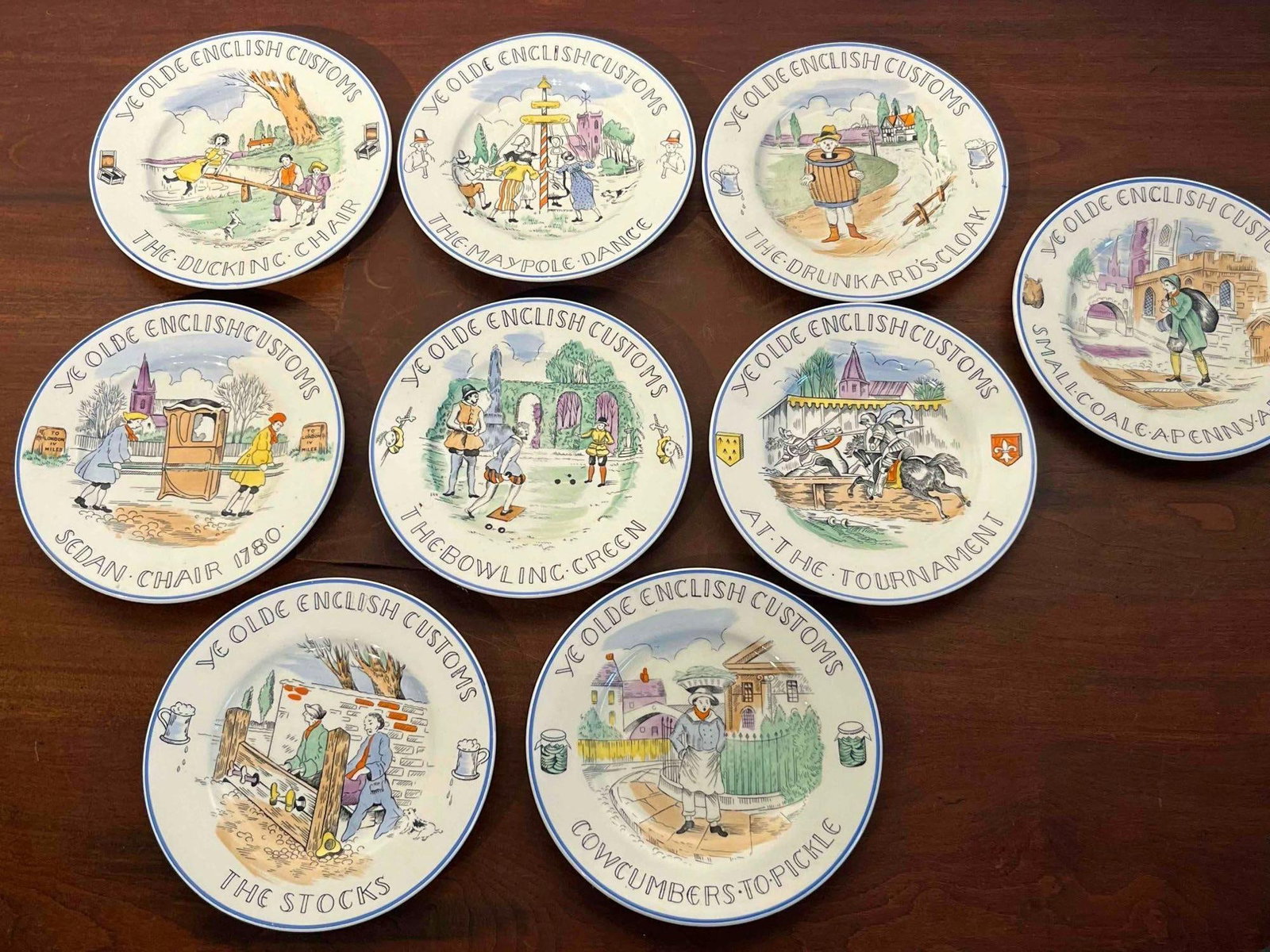 Set 9 Burgess & Leigh Customs Plates: This set of nine English earthenware tea plates features the Ye Olde English Customs pattern produced by Burgess and Leigh Ltd. Each plate is decorated with a black transfer-printed central scene