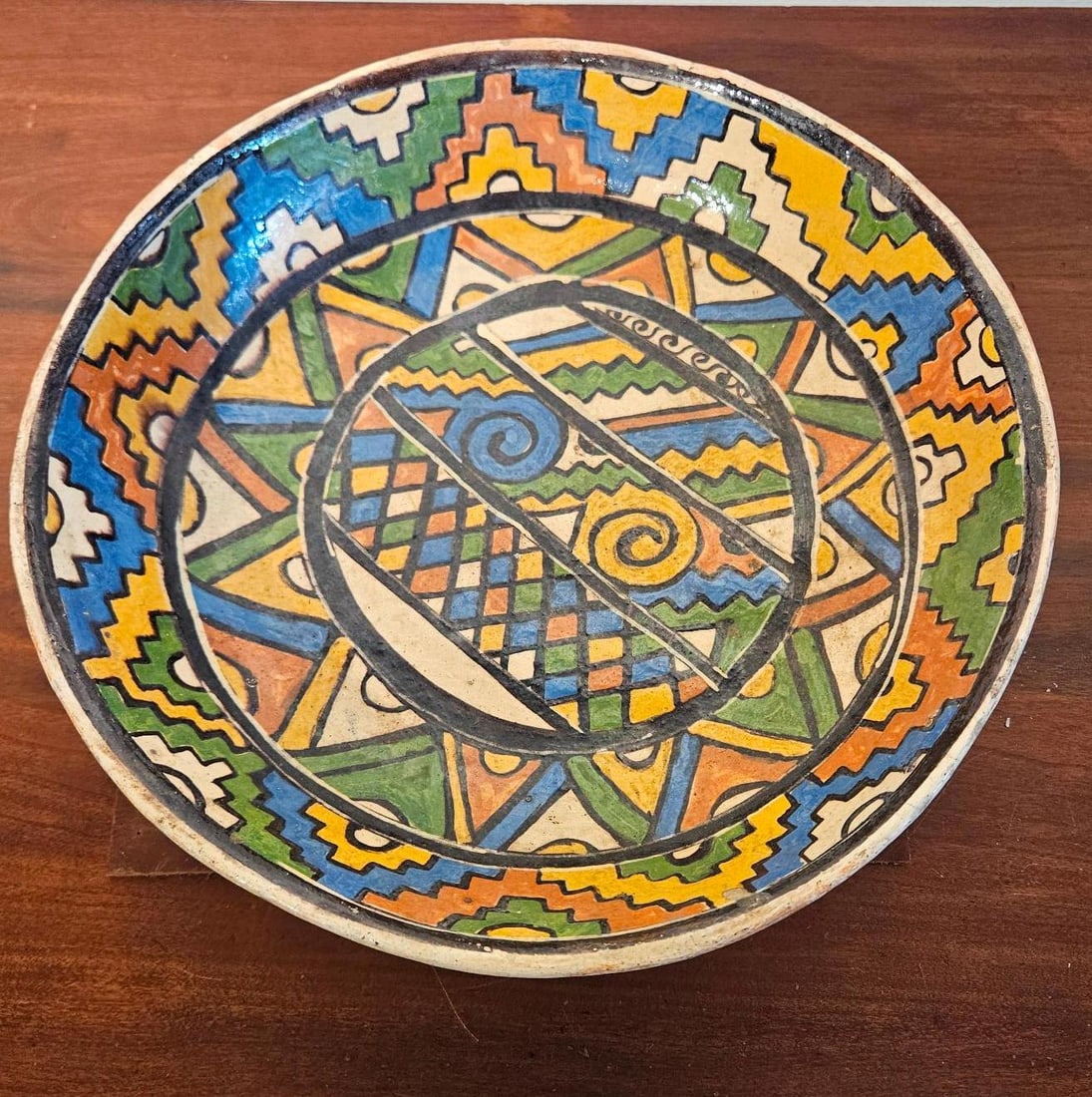 Geometric Earthenware Tripod Bowl: A large, hand-painted earthenware tripod bowl featuring vibrant geometric decoration. The interior is densely decorated with various motifs, including a central circular medallion containing spirals, 