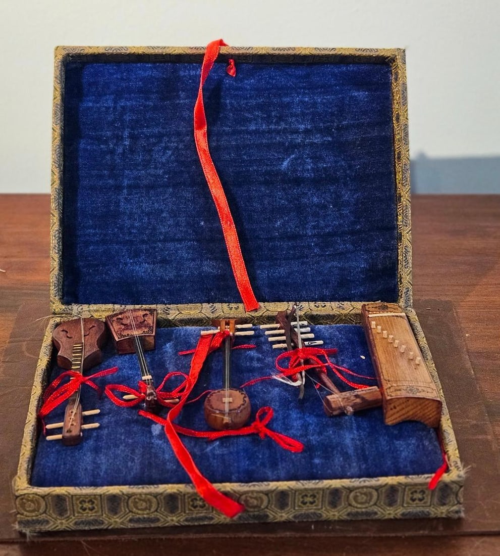 Set 5 Traditional Stringed Instruments: A set of five miniature traditional musical instruments crafted from wood with fine thread or wire strings and small pegs. The collection includes a pear-shaped lute with incised scrollwork, a square-
