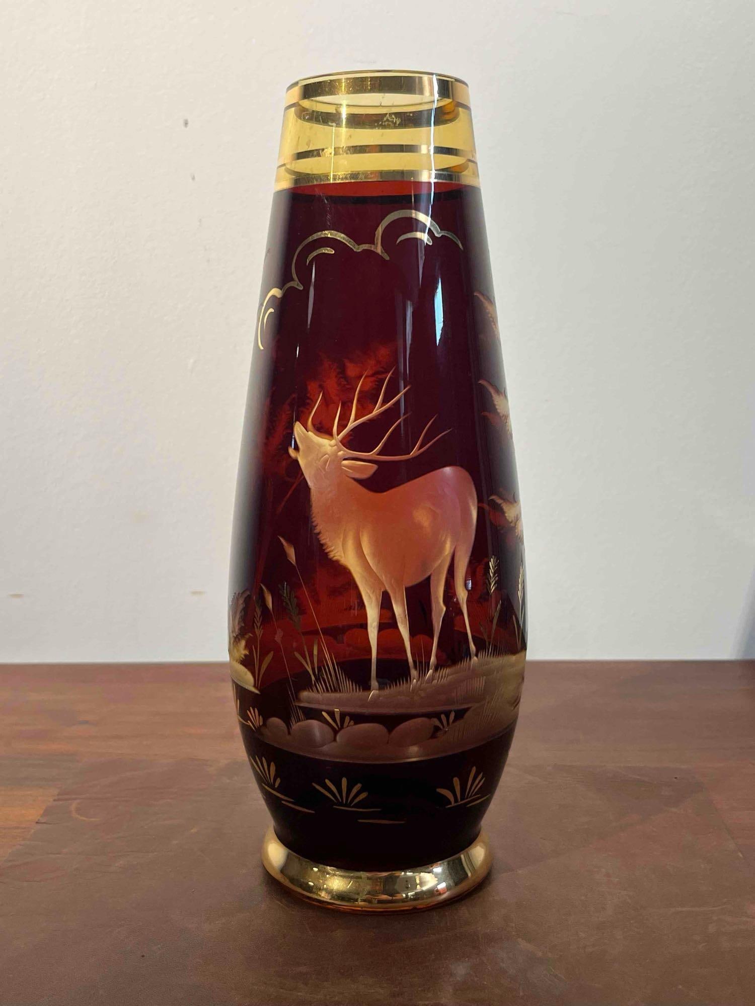Bohemian Ruby & Gilt Amber Stag Vase: A tapered Bohemian-style glass vase of elongated form, narrowing towards a footed base. The vessel is constructed from transparent amber glass with a deep ruby-red stain applied to the exterior. The c