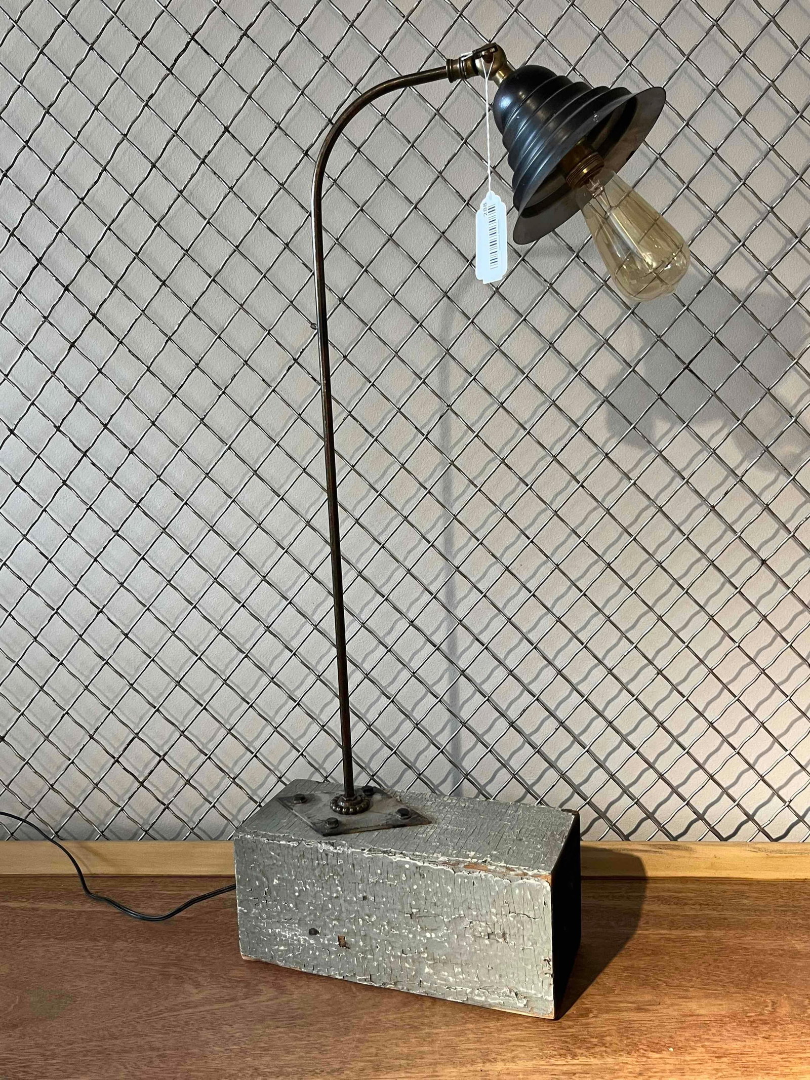 Industrial Wood & Metal Table Lamp: An industrial-style table lamp constructed from reclaimed and -inspired components. The piece features a slender, curved metal arm mounted to a substantial rectangular wooden block base. The base is f