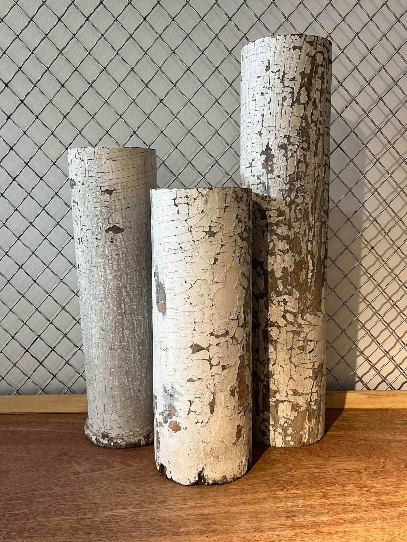Set 3 Graduated Distressed Wood Columns: Three solid wood decorative cylinders in graduated heights. Each piece is cylindrical in form with a flat-sawn top and base. One cylinder is distinguished by a turned ring molding at its base. The
