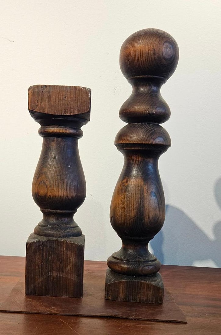 Pair Turned Wood Newel Post Elements: A pair of turned wood architectural elements, likely salvaged newel post components, featuring a dark stained or torched finish that accentuates the natural wood grain and knots. The taller element