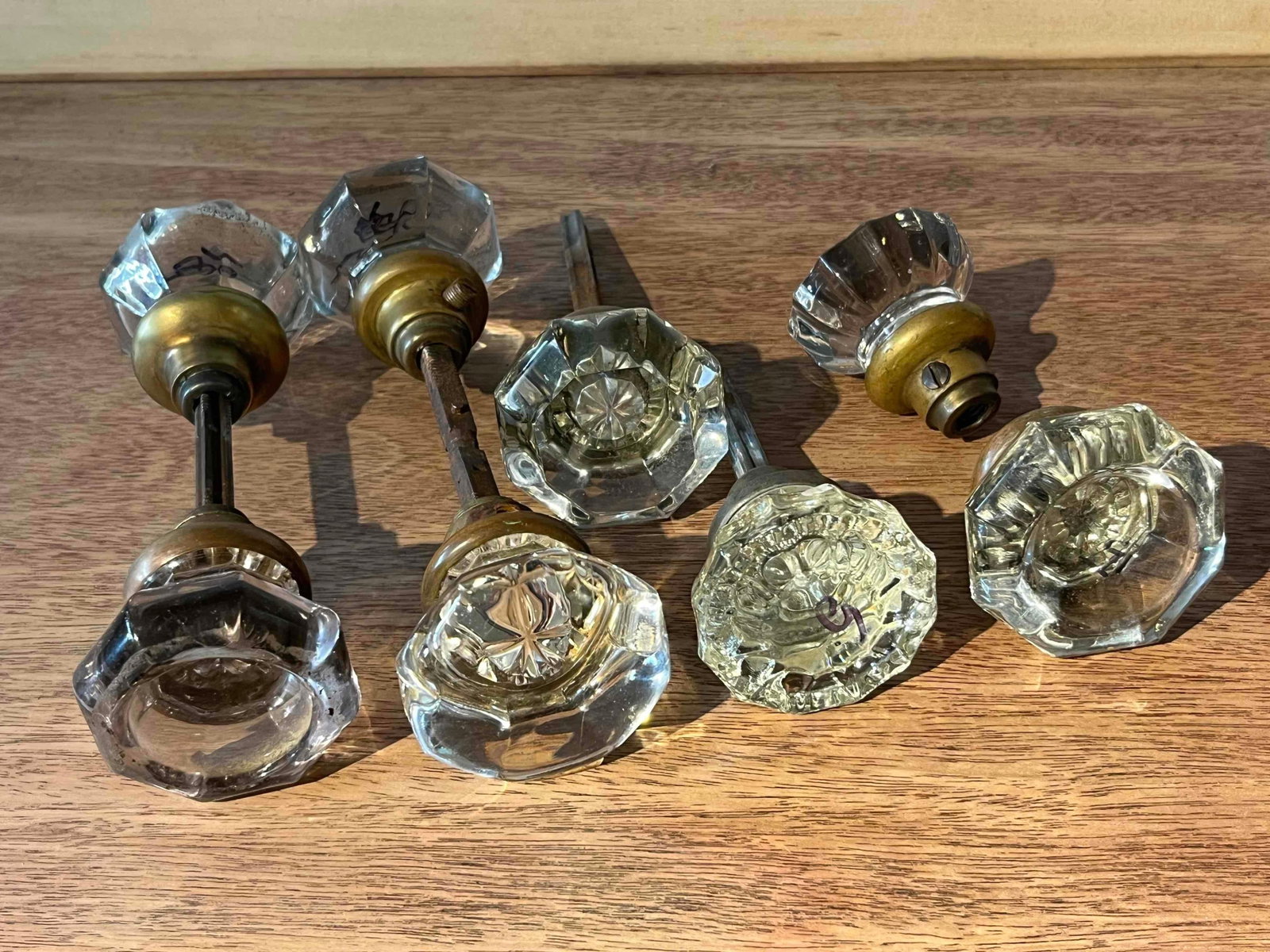 Set 8 Octagonal Fluted Glass Door Knobs: This assortment consists of eight molded glass door knobs featuring an octagonal faceted design, a style prevalent in early 20th-century American architecture. The glass components are clear with a fl