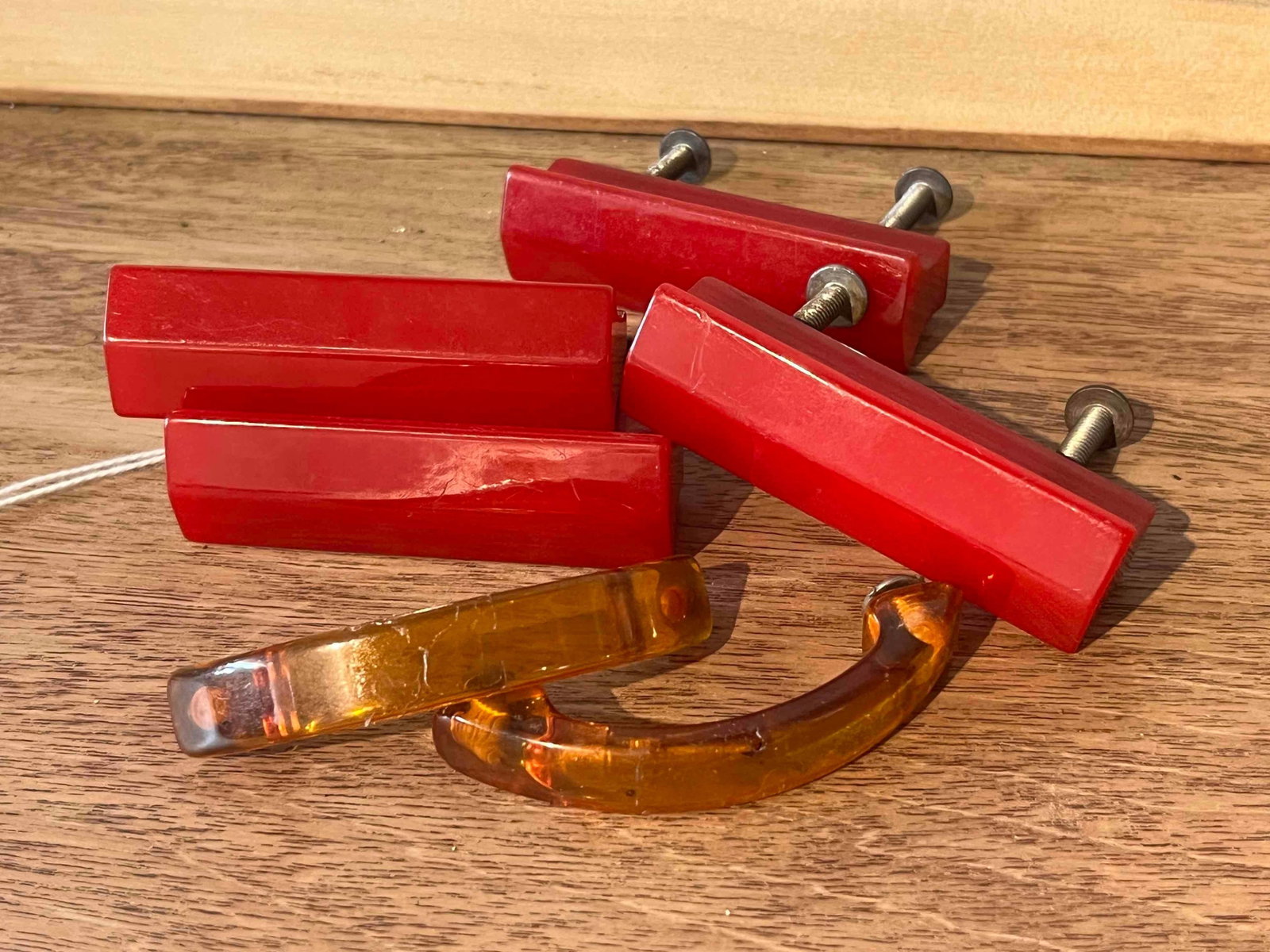 Set 6 Art Deco Bakelite & Catalin Pulls: A collection of Art Deco style furniture hardware consisting of four cherry-red rectangular pulls and two translucent amber-colored arched handles. The red pulls are manufactured from a solid
