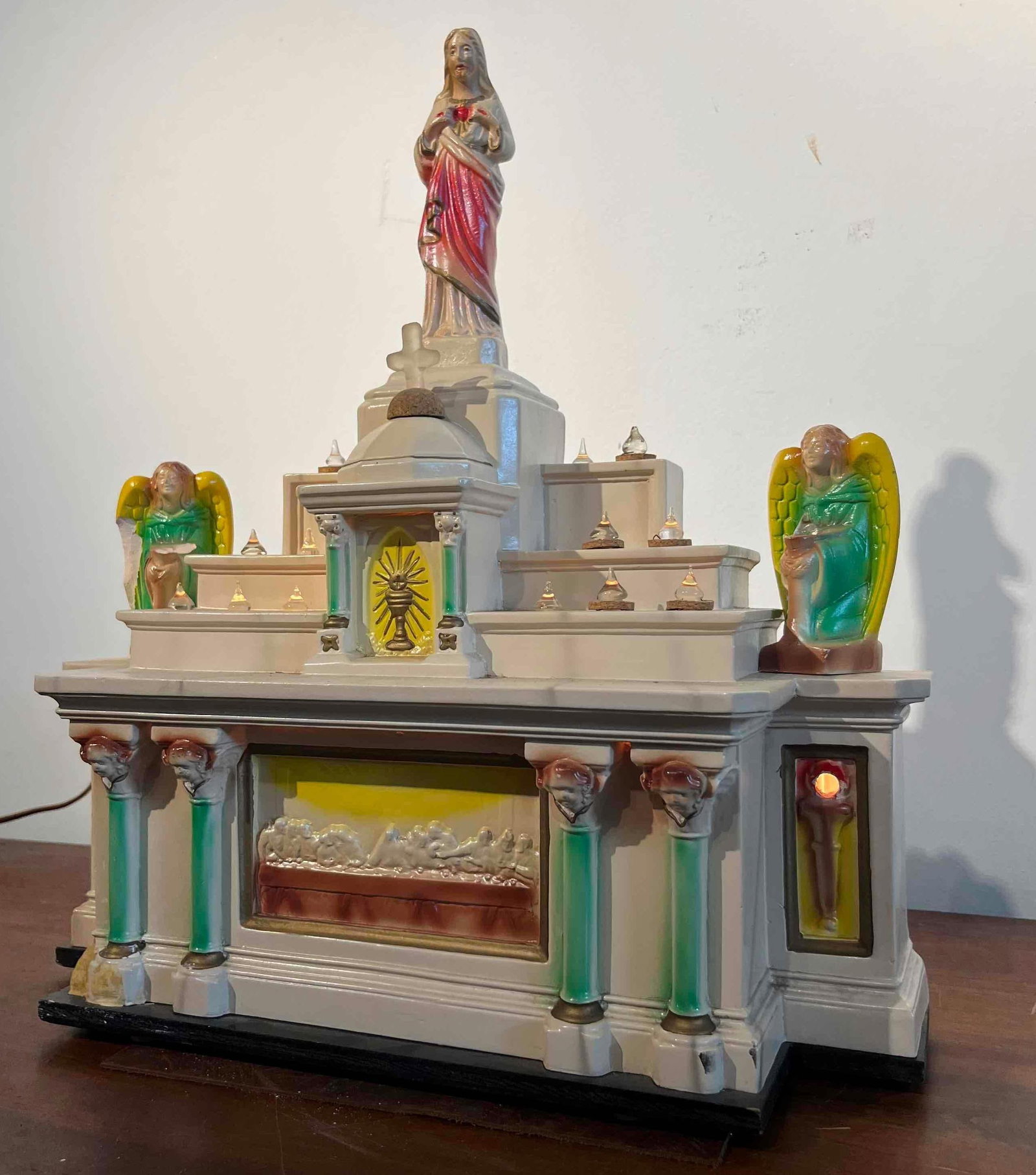 Chalkware Sacred Heart/Supper Altar: An electrified home altar shrine constructed from painted plaster, commonly referred to as chalkware, mounted upon a black-painted wooden base. The shrine features a tiered architectural composition