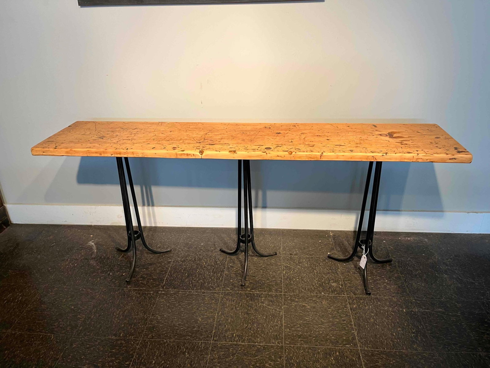 Softwood & Metal Trestle Console Table: An industrial-style long console table featuring a single thick, solid softwood top with a heavy, character-rich patina. The rectangular tabletop is supported by three black-painted metal tripod bases